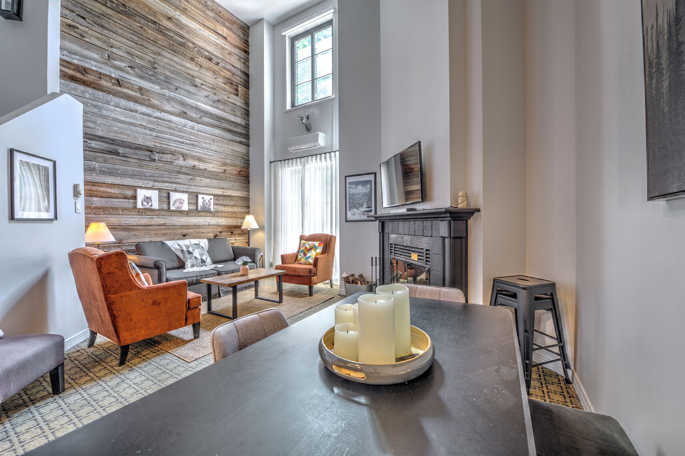 A modern living room with a fireplace, wooden wall paneling, and a dining area with candles.