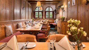 Ein Restaurant mit Holzwänden, einem langen Esstisch für mehrere Gäste und Blick auf Bäume durch große Fenster.