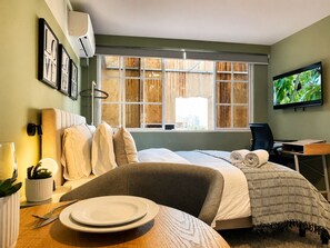 A hotel room with a bed, a desk, a television, and a window with a view of the city. - Old Town Apartment | Perfect for exploring on foot (Panamá)