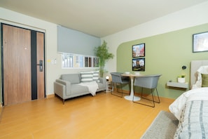 A modern room with a sofa, a small table, a chair, a bed, a plant, and a window with blinds. - Old Town Apartment | Perfect for exploring on foot (Panamá)