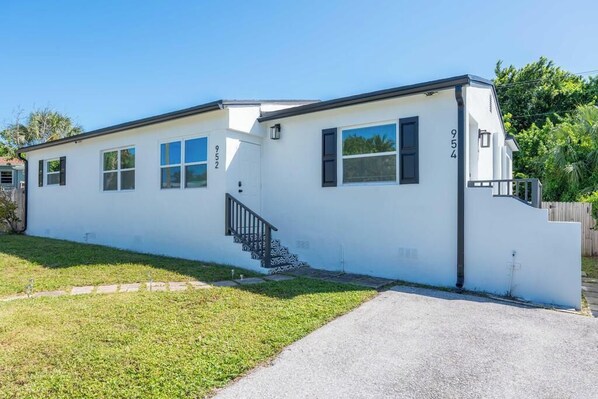 A single-story white building with a black staircase, numbered 954, and a small front yard. - 3BR/2BA - King Bed - Short drive to Downtown, Northwood, PBI Airport & Beaches (West Palm Beach)