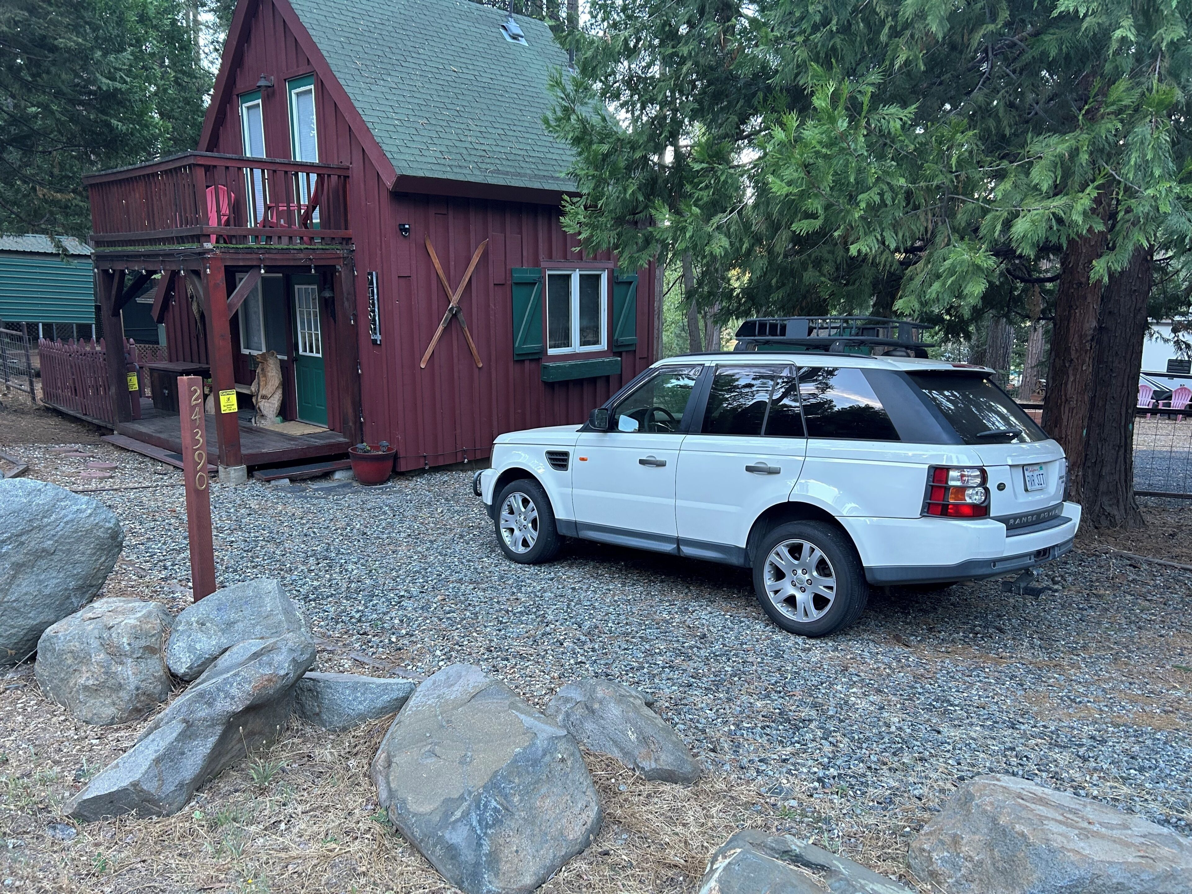 A white Range Rover parked in front of a red wooden building with a gravel driveway and large rocks.