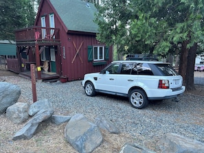 A white Range Rover parked in front of a red wooden building with a gravel driveway and large rocks.