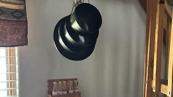 A kitchen with a stove, a hanging pot rack, and a wooden shelf with bottles.
