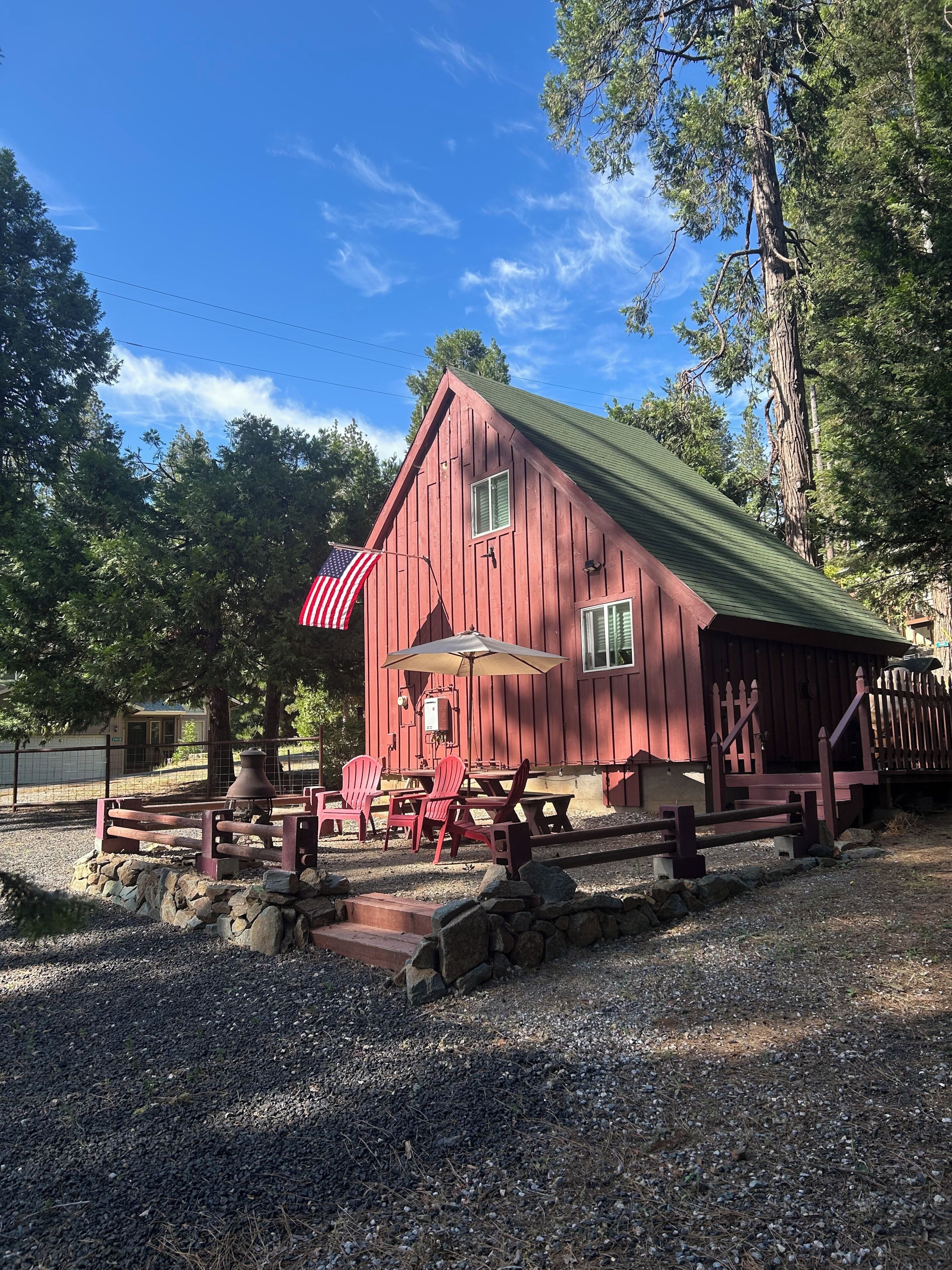 A red barn with a green roof, outdoor seating, and an American flag.