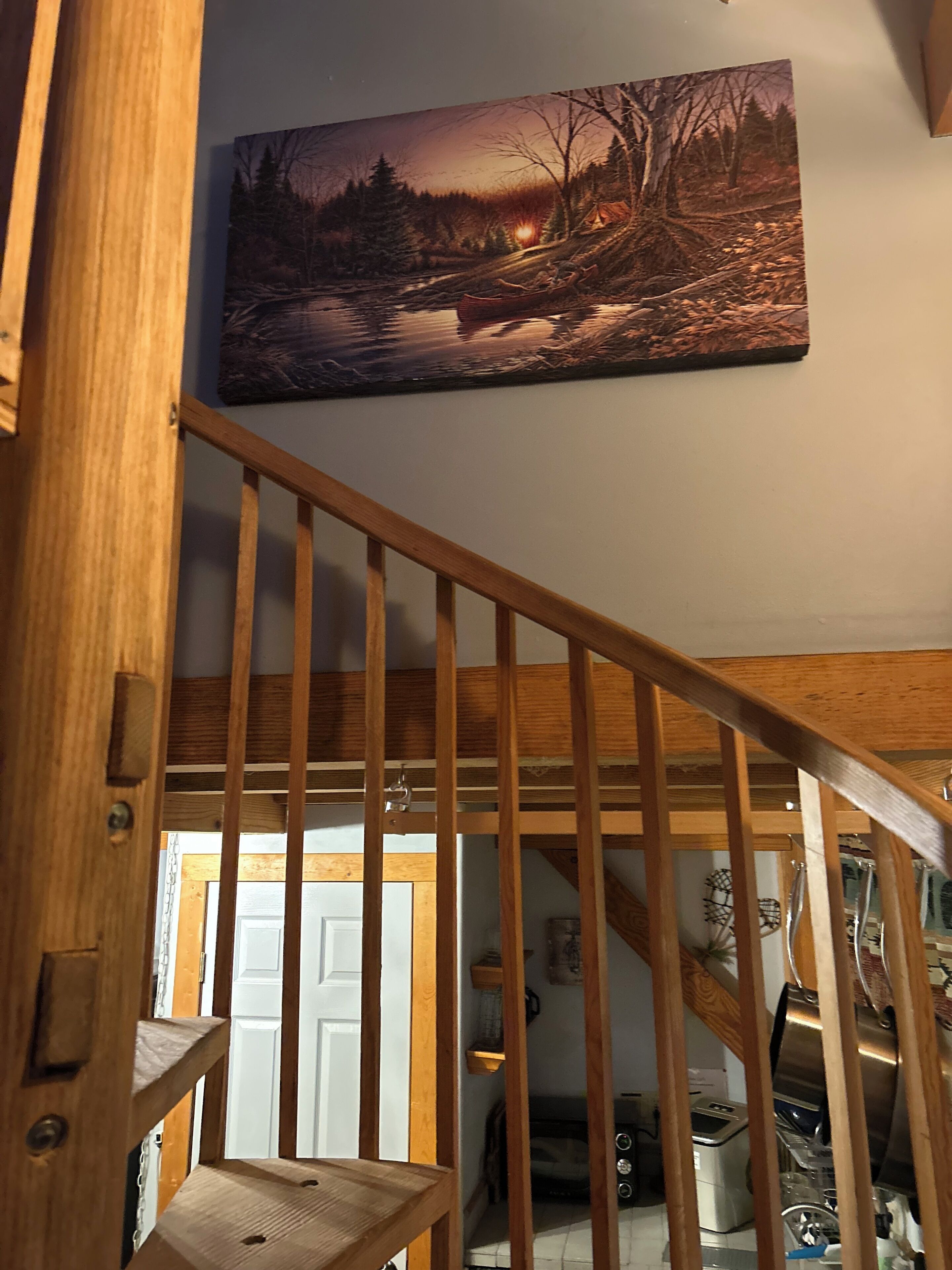 A wooden staircase leading to a second floor, with a painting of a forest scene above.