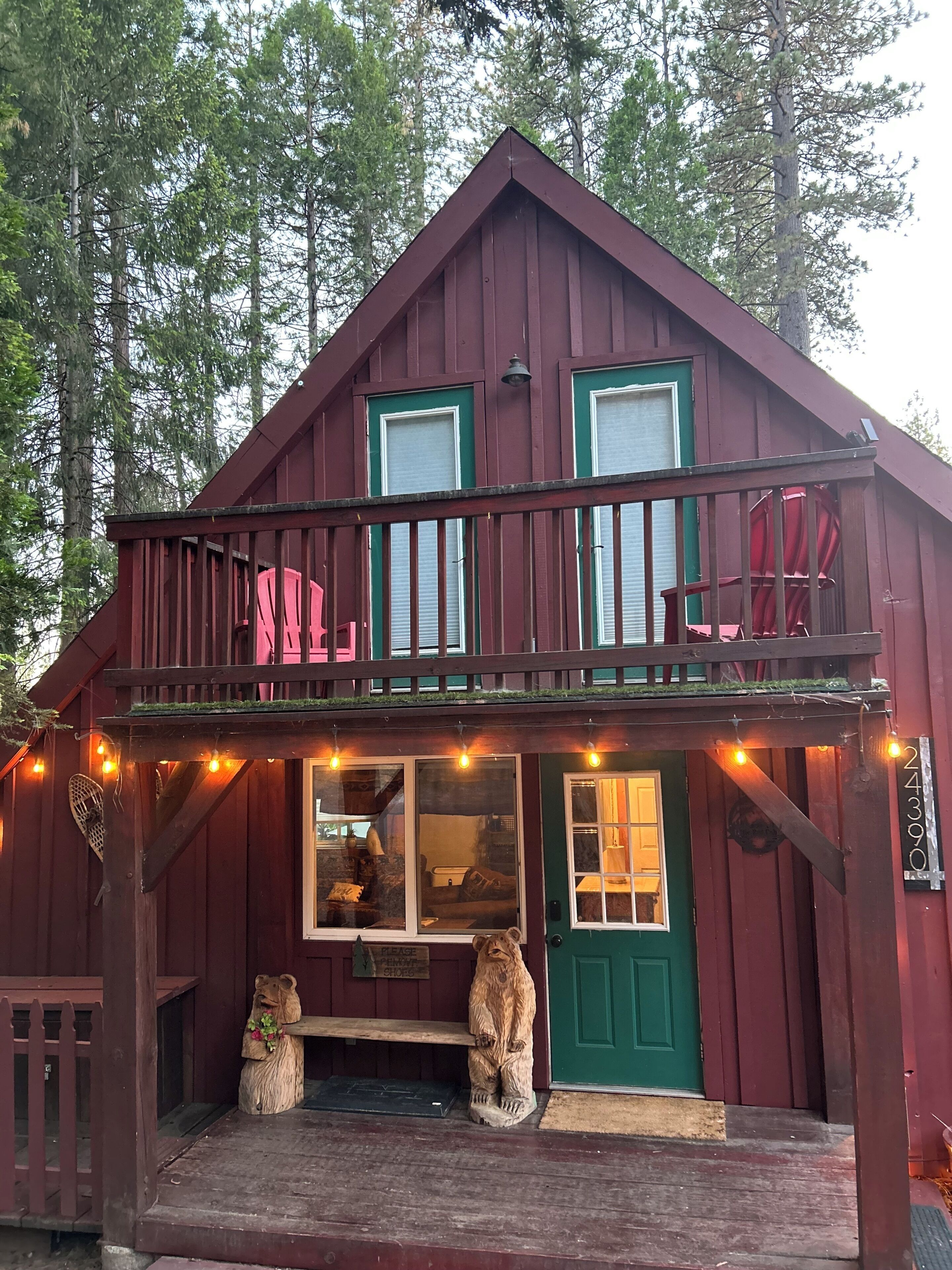 A two-story wooden cabin with a balcony, a green door, and a small front porch with a bear statue.