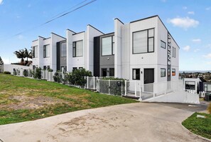 A modern multi-story building with a white exterior, large windows, and a gated entrance. - Sunny 3BR Retreat Browns Bay Beach Zodiak Stays (Auckland  Central)