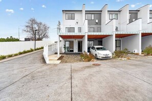A modern two-story building with a white exterior, a covered carport, and a paved driveway. - Sunny 3BR Retreat Browns Bay Beach Zodiak Stays (Auckland  Central)