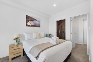 A bedroom with a bed, a nightstand, a painting, a shower, and a door. - Sunny 3BR Retreat Browns Bay Beach Zodiak Stays (Auckland  Central)
