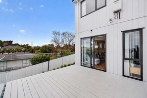 A modern residential building with a balcony, a sliding glass door entrance, and a visible interior with a dining area. - Sunny 3BR Retreat Browns Bay Beach Zodiak Stays (Auckland  Central)
