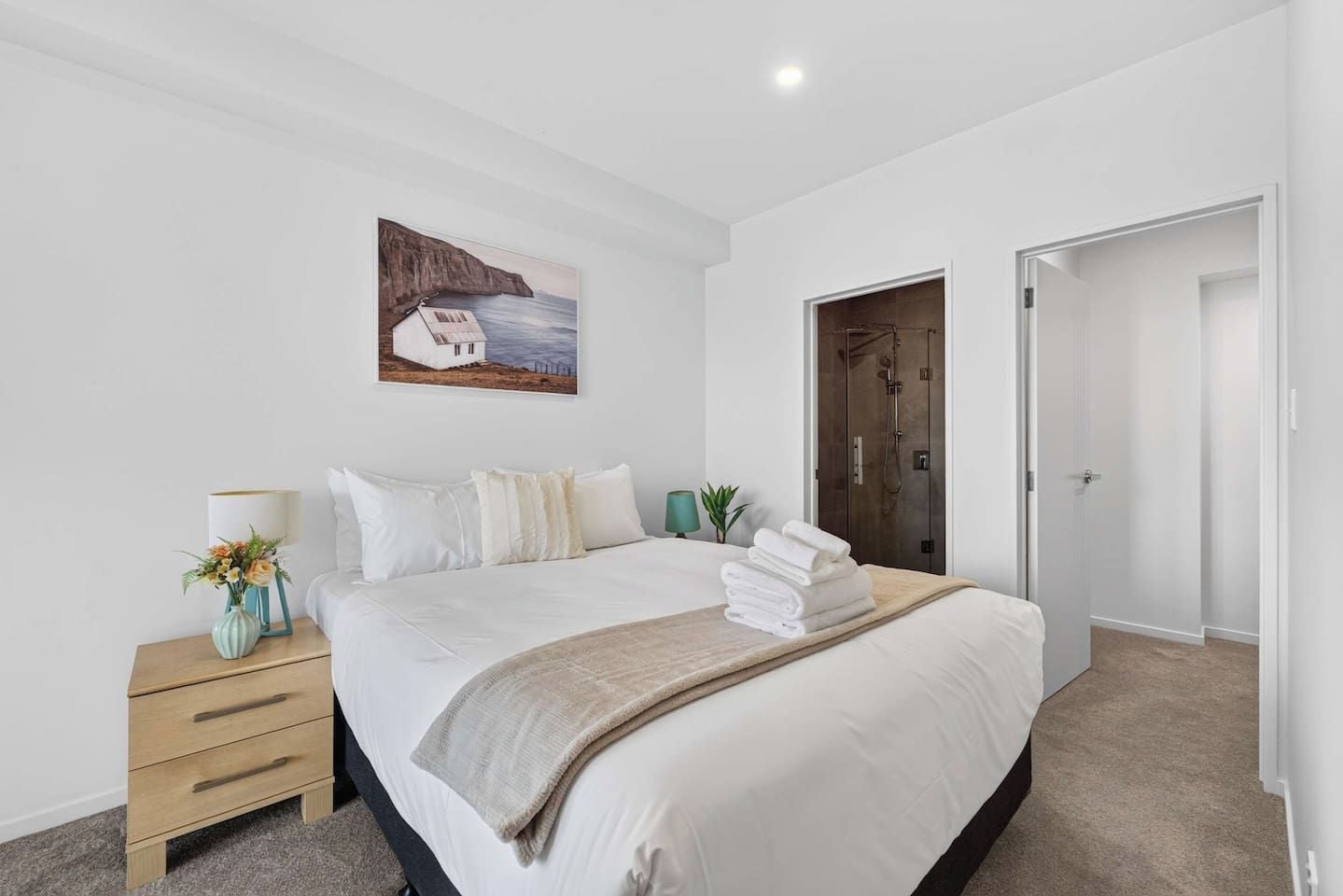 A bedroom with a bed, a nightstand with a lamp, a painting, and a shower area.