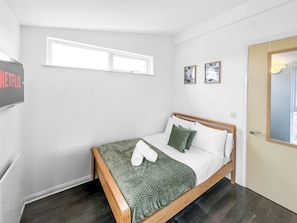 Een slaapkamer met een bed, een raam, een deur en een aan de muur bevestigde televisie.