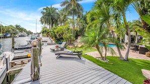 Eine Holzterrasse mit Liegestühlen, einem Pool und Palmen.