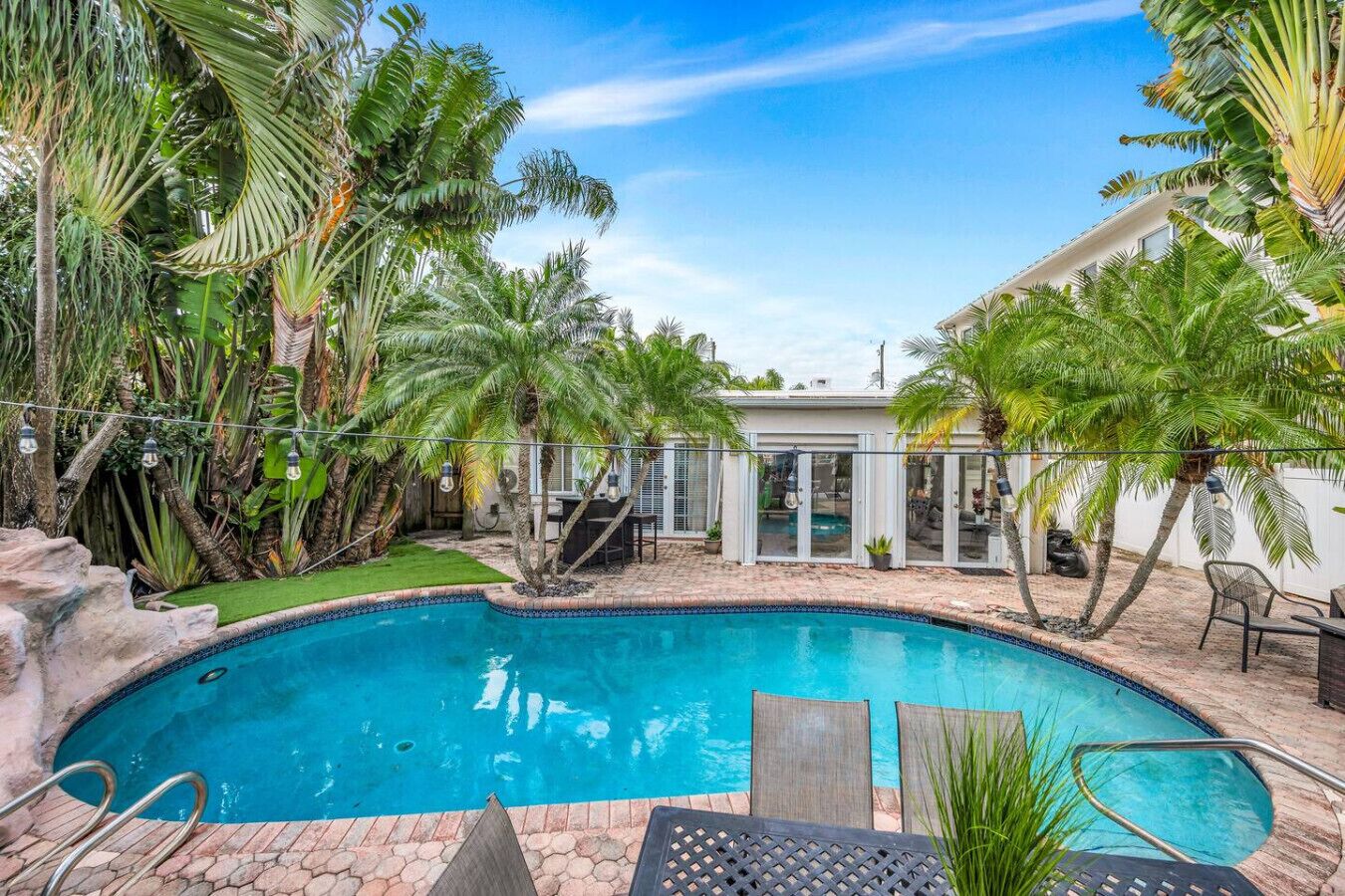 Quintal com piscina, cercado por palmeiras e uma casa.