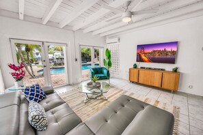 Un salon moderne avec un canapé, une table basse en verre, un téléviseur et une vue sur la piscine.