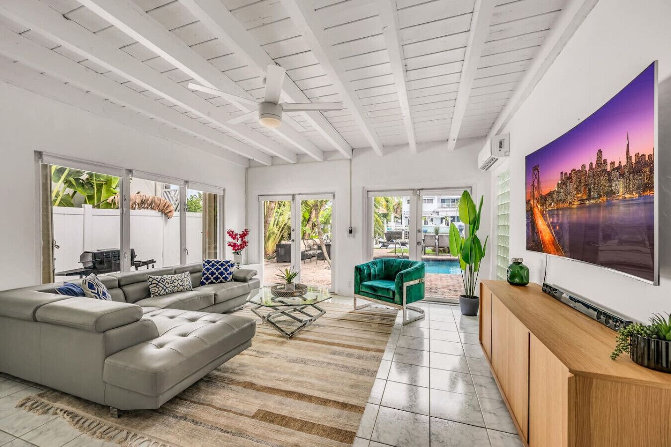 A modern living room with a grey sofa, a green armchair, a glass coffee table, and a TV on a wooden cabinet.