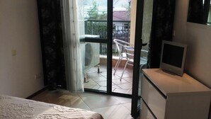 Ein Schlafzimmer mit einem Bett, einem Fernseher auf einem kleinen Tisch, einem Balkon mit einem Stuhl und einer Glastür.