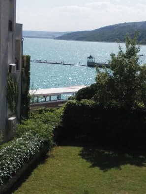 A view of a lake with a pier and a gazebo, surrounded by greenery and a building. - Apartment Sleeps 2 with Pool & Balcony (Balchik)
