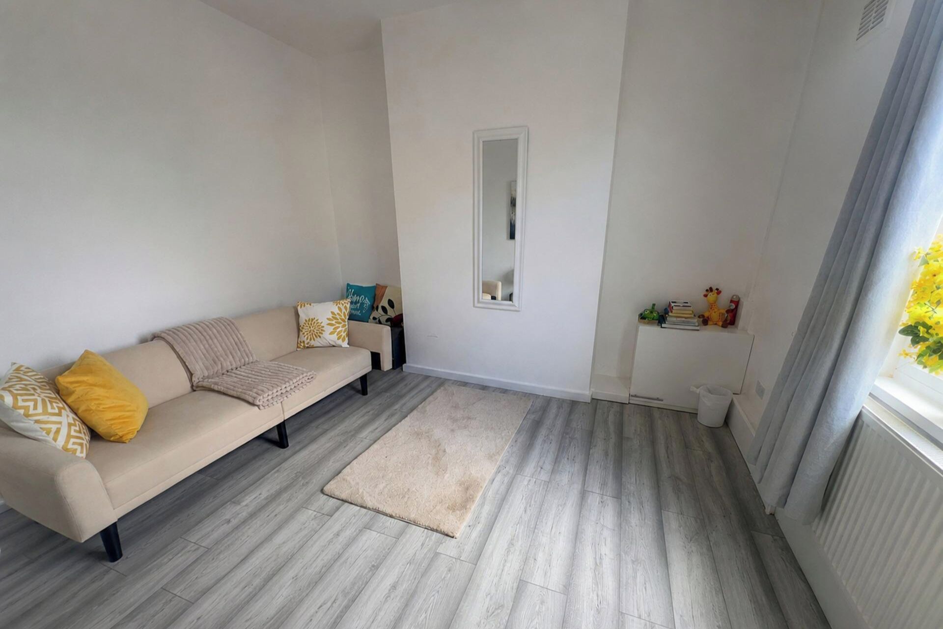 A living room with a beige sofa, a small rug, and a window with curtains.