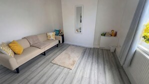 Een woonkamer met een beige bank, een kleedje en een raam met gordijnen.