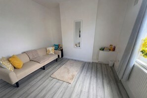 Ein Wohnzimmer mit einem beigen Sofa, einem kleinen Teppich und einem Fenster mit Vorhängen.