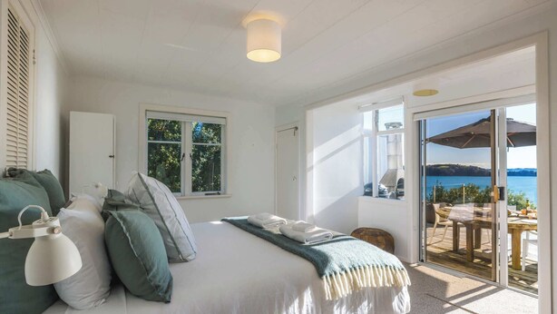 Quarto com cama, almofadas, luminária, janela e vista para o exterior.
