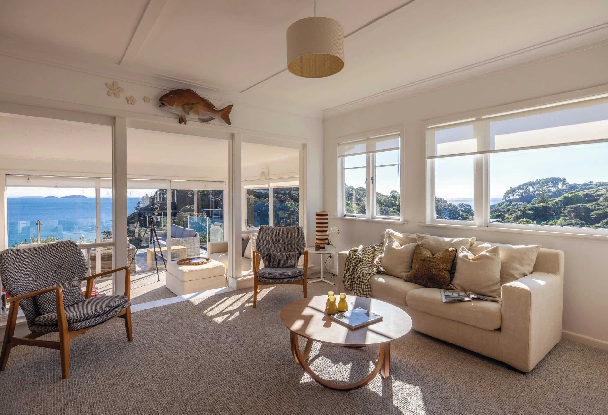 A spacious living room with a sofa, two chairs, a coffee table, and large windows offering a view of the landscape.