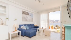 Een moderne woonkamer met een blauwe bank, een witte bijzettafel, een lamp en een schilderij aan de muur.