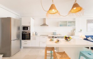 A modern kitchen with stainless steel appliances, a central island with stools, and a hanging light fixture.