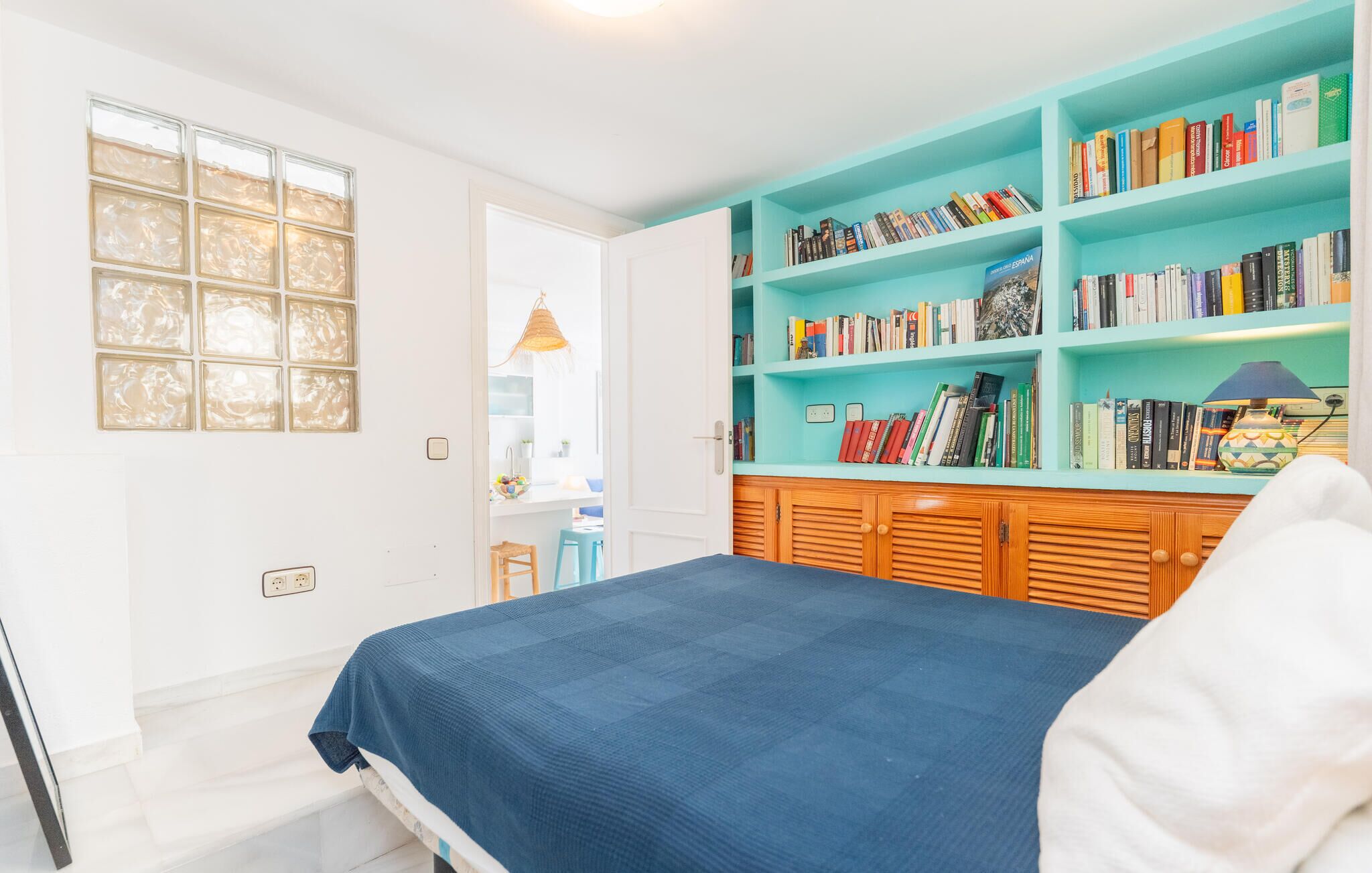 A bedroom with a bed, a bookshelf, and a window.