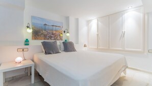 Een slaapkamer met een groot bed, een nachtkastje met een lamp, een aan de muur hangend schilderij en een kledingkast.