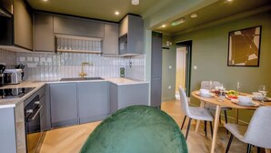 Eine moderne Küche mit grauen Schränken, einem eingebauten Backofen und einem Essbereich mit rundem Tisch, gedeckt für vier Personen.