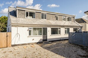 A two-story residential building with a sloped roof, multiple windows, and a gravel driveway. - 1 Bedroom Apartments Sleeps 3 - Balcony - Pets Ok (St. Ives)