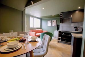 A modern kitchen with a dining area, a green sofa, and a kitchen island with a sink and stove. - 1 Bedroom Apartments Sleeps 3 - Balcony - Pets Ok (St. Ives)