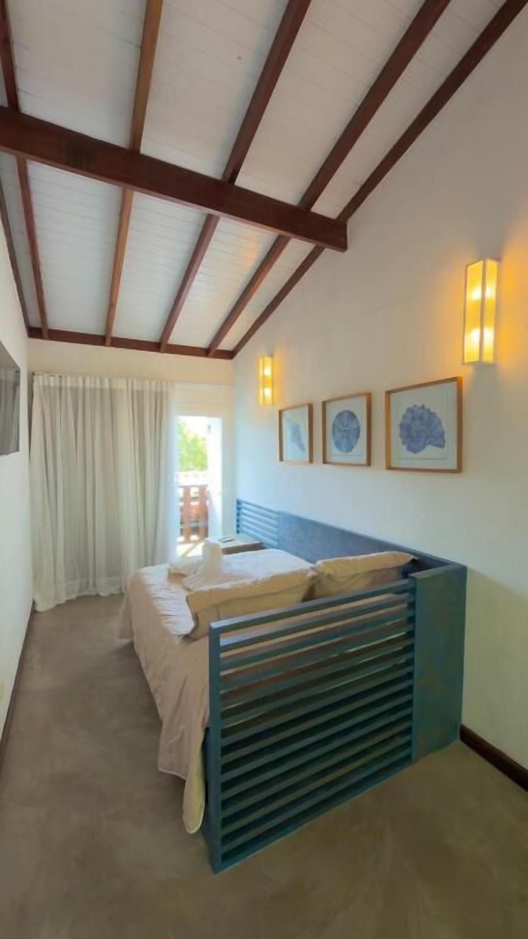 Un dormitori amb un llit, una finestra amb cortines, una làmpada de paret i quadres emmarcats.
