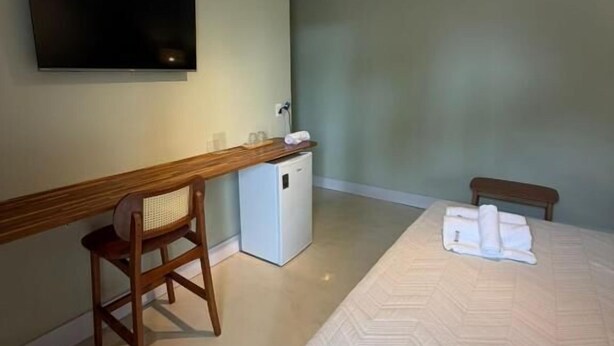A hotel room with a bed, a desk, a chair, a television, and a small refrigerator. - Casa Canoa Frente Mar e Alta Gastronomia (Guarujá)
