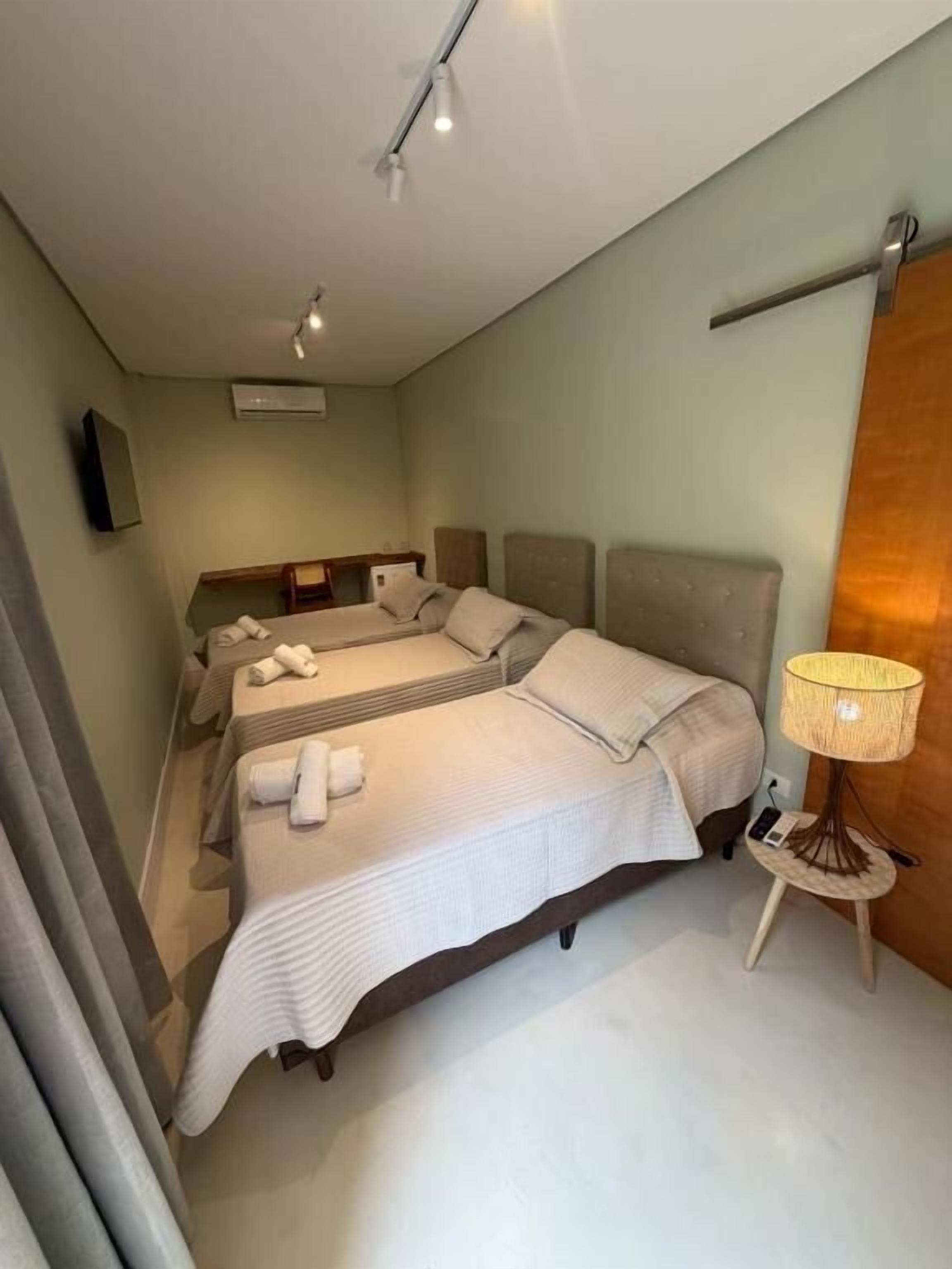 A hotel room with two beds, a small table with a lamp, and a wall-mounted TV.