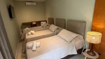 A hotel room with two beds, a small table with a lamp, and a wall-mounted TV.