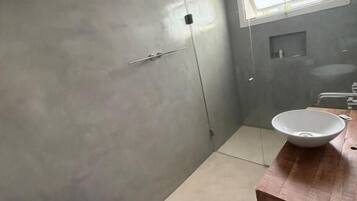 Un baño moderno con un espejo grande, un tocador de madera, un lavamanos blanco y una zona de ducha.