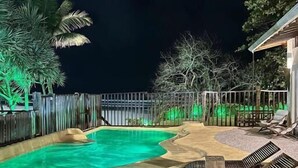 A swimming pool with a curved design, surrounded by lounge chairs and a wooden deck. - Casa Canoa Frente Mar e Alta Gastronomia (Guarujá)