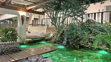 An outdoor garden with a pond, wooden deck, and tropical plants.