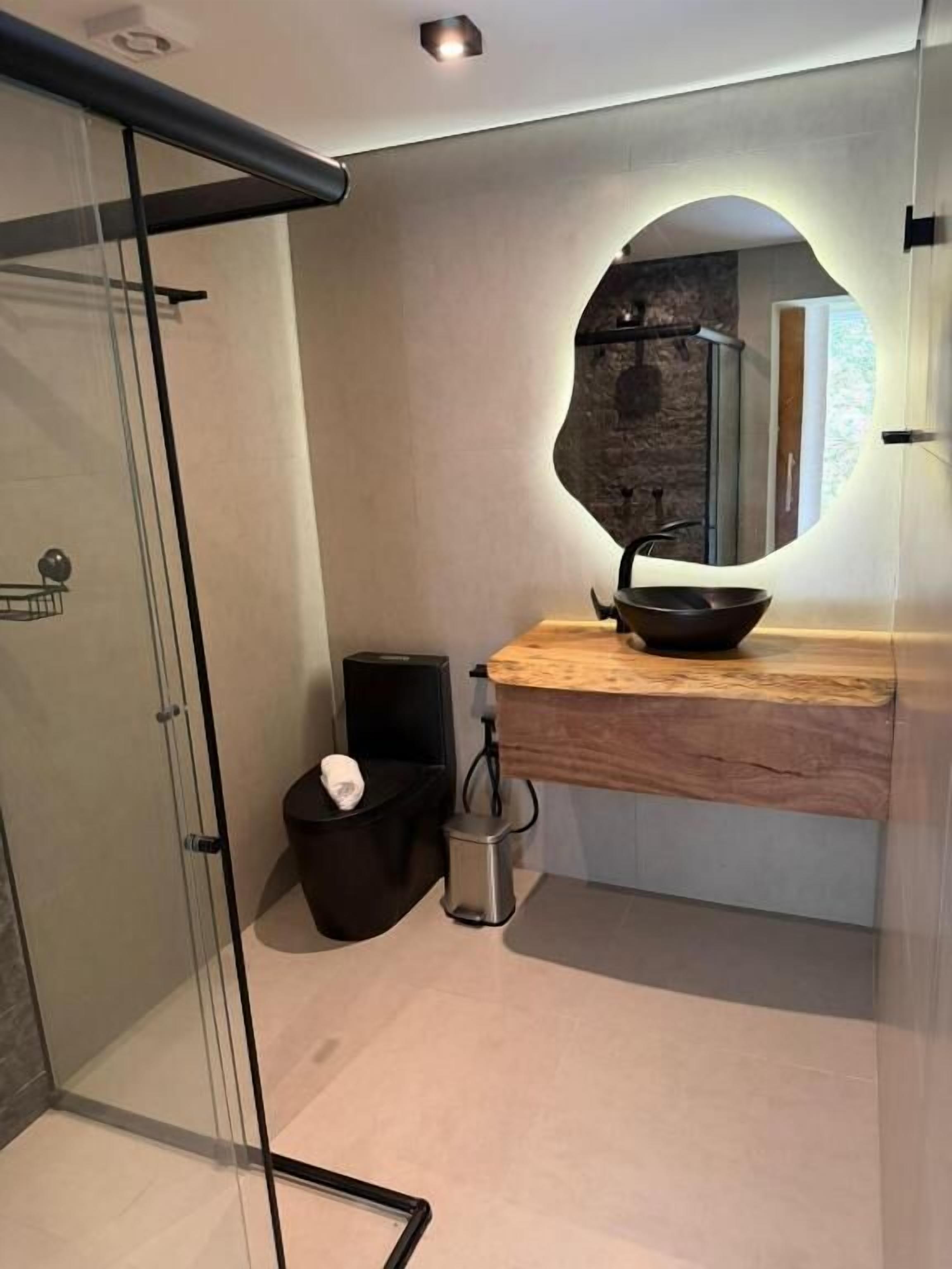 Un bagno moderno con box doccia in vetro, un mobile lavabo in legno con lavabo nero e una parete in pietra.