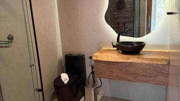 Un bagno moderno con box doccia in vetro, un mobile lavabo in legno con lavabo nero e una parete in pietra.