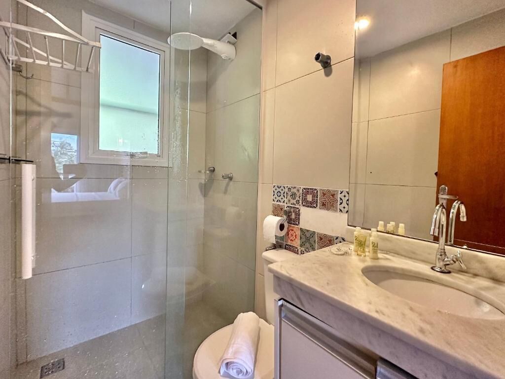 Un baño con ducha de vidrio, inodoro, lavabo con espejo y toalla.