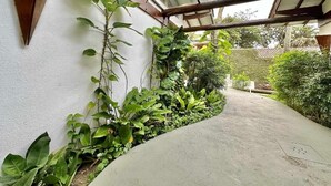 A covered outdoor area with a concrete path, surrounded by various plants and a white wall. - Casa Canoa Frente Mar e Alta Gastronomia (Guarujá)
