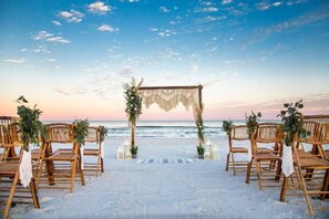 Montaje para una boda en la playa con un dosel, sillas y vista al océano.