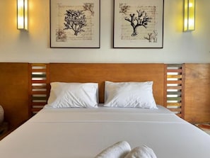 A hotel room with a large bed, two wall-mounted light fixtures, and framed botanical artwork.
