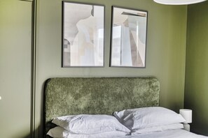 Habitación de hotel con una cama, almohadas, una mesita de noche, una lámpara y dos cuadros abstractos en la pared.