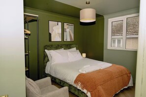 A bedroom with a bed, a chair, a bedside table, a lamp, and a window with blinds. - 1 Bedroom Apartment Sleeps 2 - Pets Welcome (St. Ives)